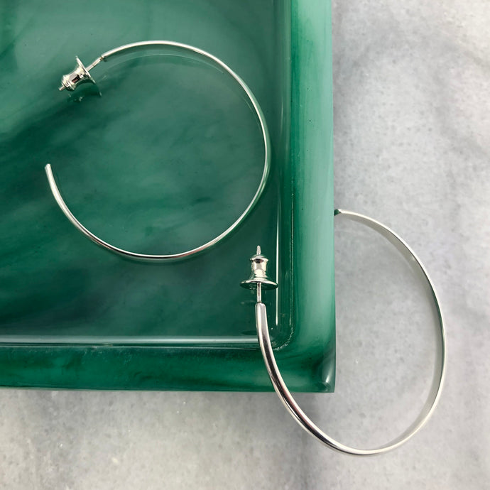 Large round silver post hoop earrings on green jewelry tray and marble